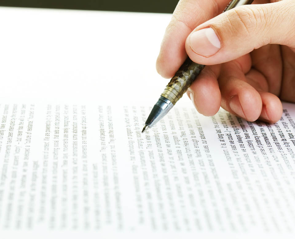 Close-up of male hand following text on paper with a pen